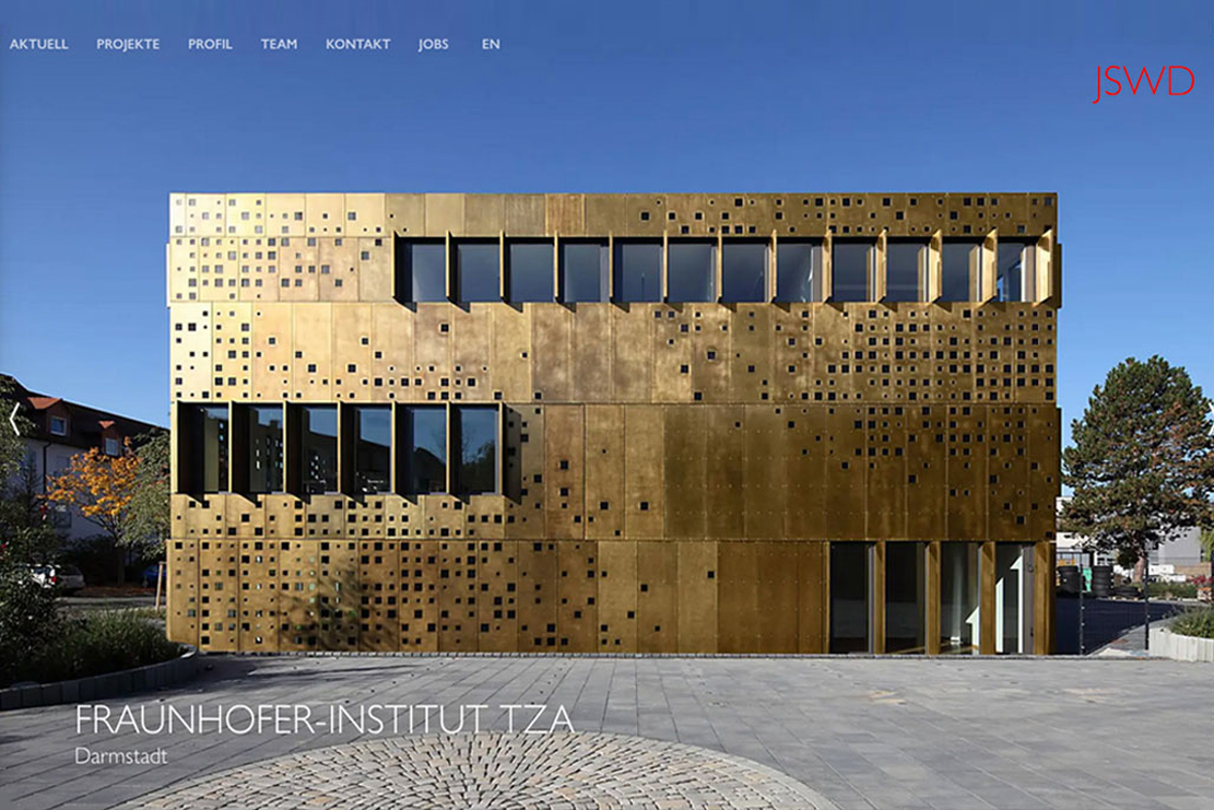 Bildbeschreibung: Einer der Teaser der Start Webseite JSWD mit einem grossen rechteckigen Gebäude, dem Transferzentrum Adaptronik am Fraunhofer-Institut LBF, mit einer Fassade aus regelmäßig perforierte Messingbond-Tafeln, die mit changierenden Farben auf die Lichtverhältnisse reagieren. Für den Relaunch der Webseite JSWD Architekten, Konzept und Design von Minkdesign.  